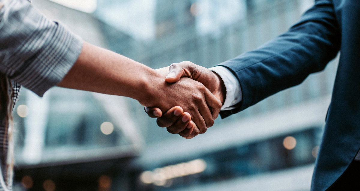 Two individuals shaking hands in a business setting, with a blurred urban background.