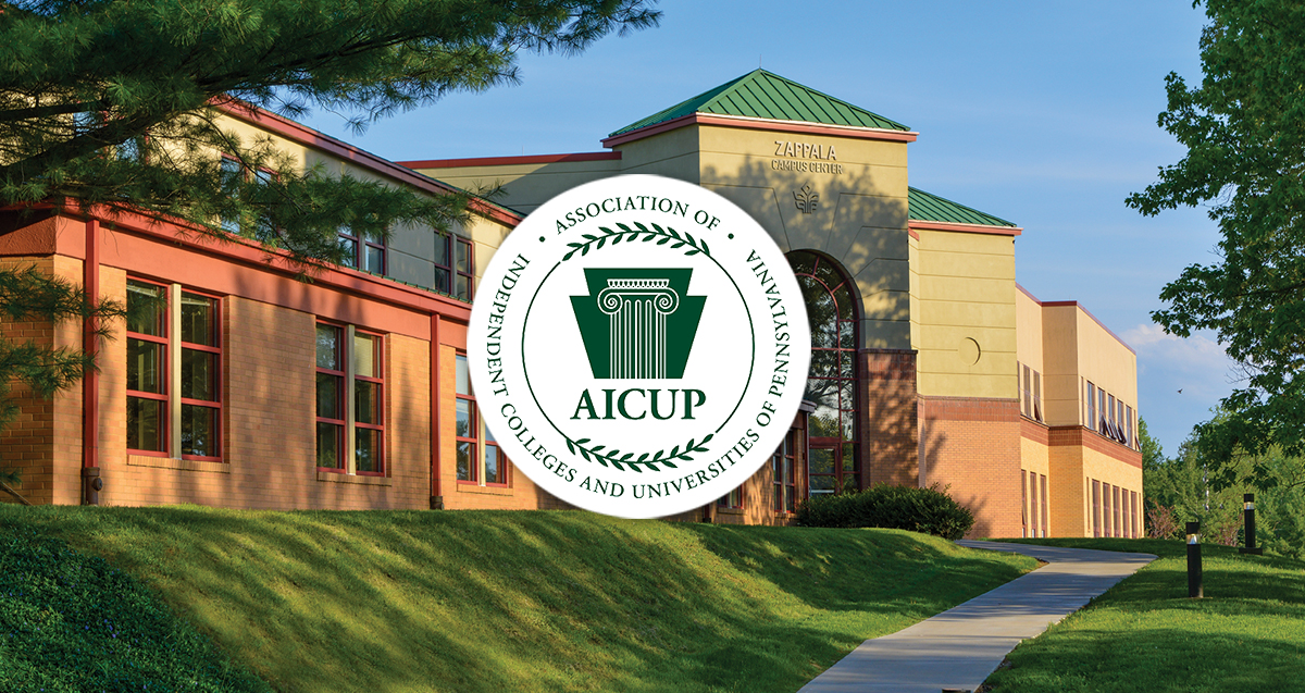 Exterior view of La Roche University's Zappala Campus Center building with a logo of the Association of Independent Colleges and Universities of Pennsylvania (AICUP) prominently displayed, surrounded by lush greenery and a clear sky.