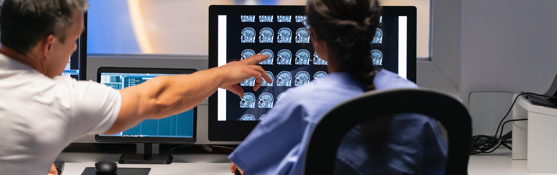 Two medical professionals analyze brain scans on a computer screen in a dimly lit room.