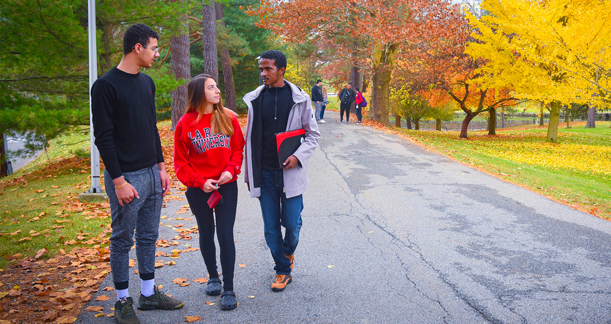 Three La Roche University students walking and conversing on a campus path lined with autumn trees. 