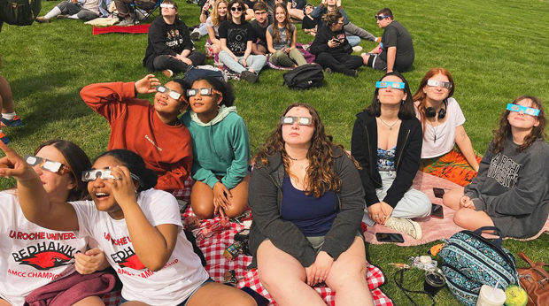 La Roche University student sit on the campus lawn watching the solar eclipse.