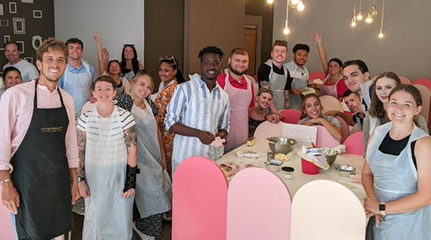 Group of La Roche University students participating in a cooking class, smiling and posing for a photo around a table with kitchen utensils and ingredients.