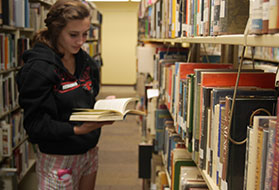 Female student standing in isle of books reading