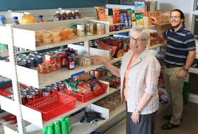 Two La Roche University employees stand next to stocked shelves for the Providence Food Pantry on campus.