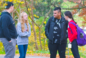Four La Roche University students converse outside on a fall day.