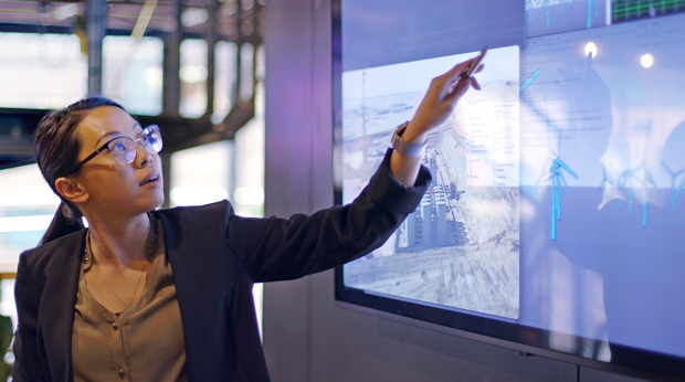 Person in a business suit pointing at a large digital screen displaying graphs and data analytics.