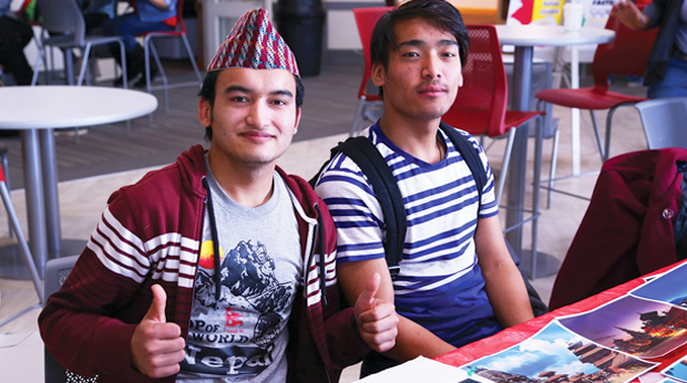 Two students sit at a table for International Education Month at La Roche University. One student is giving a thumbs up.
