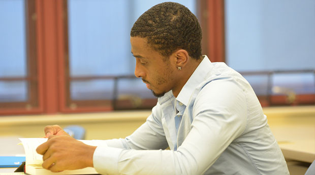 A student sits at a desk reading a book in a classroom.