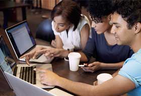 Three students gathered around two laptops
