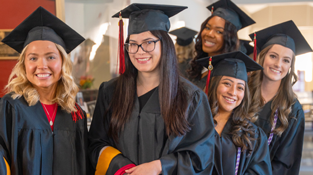 Five La Roche University graduates wearing their caps and gowns at commencement.