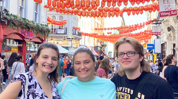 Three La Roche students in Chinatown, smiling with red lanterns hanging above the busy street.