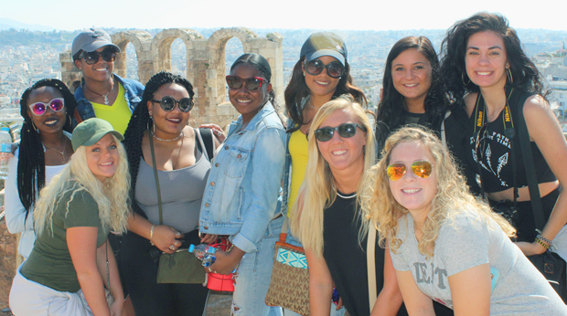 Group of La Roche students smiling at the camera with the ancient ruins of the Acropolis in Athens visible in the background.