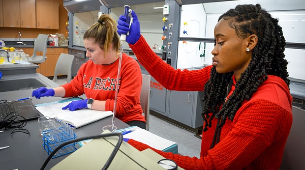 Two students perform an experiment in the science laboratory at La Roche University. One is holding instrumentation and the other is looking at a laptop.