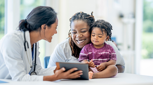 A medical provider talks to a mother and child. The provider is holding a notepad.