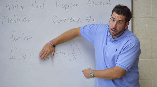 A mathematics professor at La Roche University teaches in front of a white board. The board has equations and words written on it.