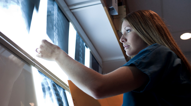 A medical imaging professional looks at X-rays on a light box.