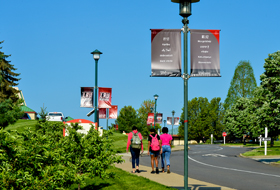 Group of La Roche University students walk on a sidewalk from the commuter parking lot to upper campus on a summer day.