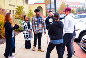 Four La Roche University students in a residence hall room. Two are studying at a desk and the other two are playing video games.