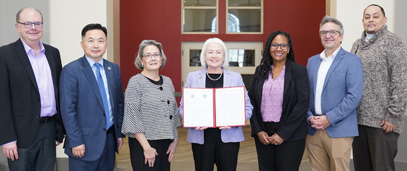 A crowd of prospective students and parents at an Open House event at La Roche University. There are tables covered in red tablecloths with various brochures and fliers laid out on top. There are professors and students conversing in the background.