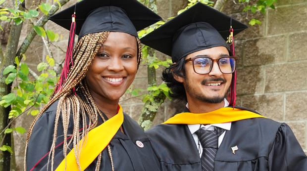 Two students smile while wearing academic regalia.